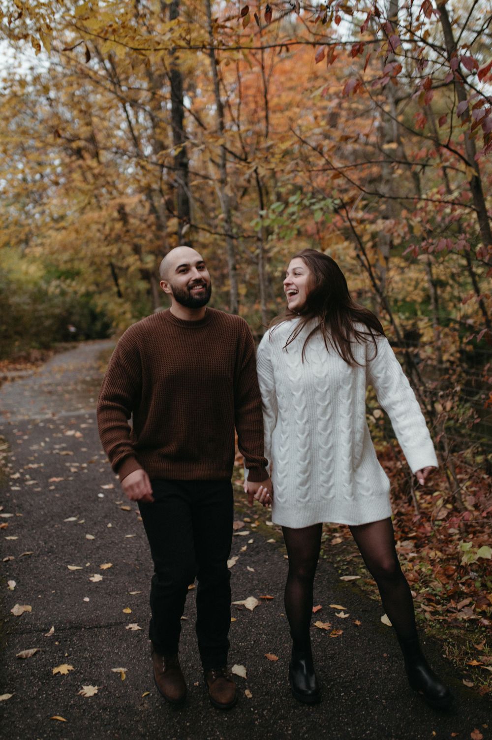 A couple walking and laughing together on a path lined with autumn trees.