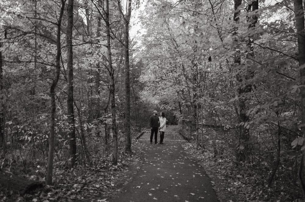A black and white photo of a wooded trail with silhouettes walking in the distance.