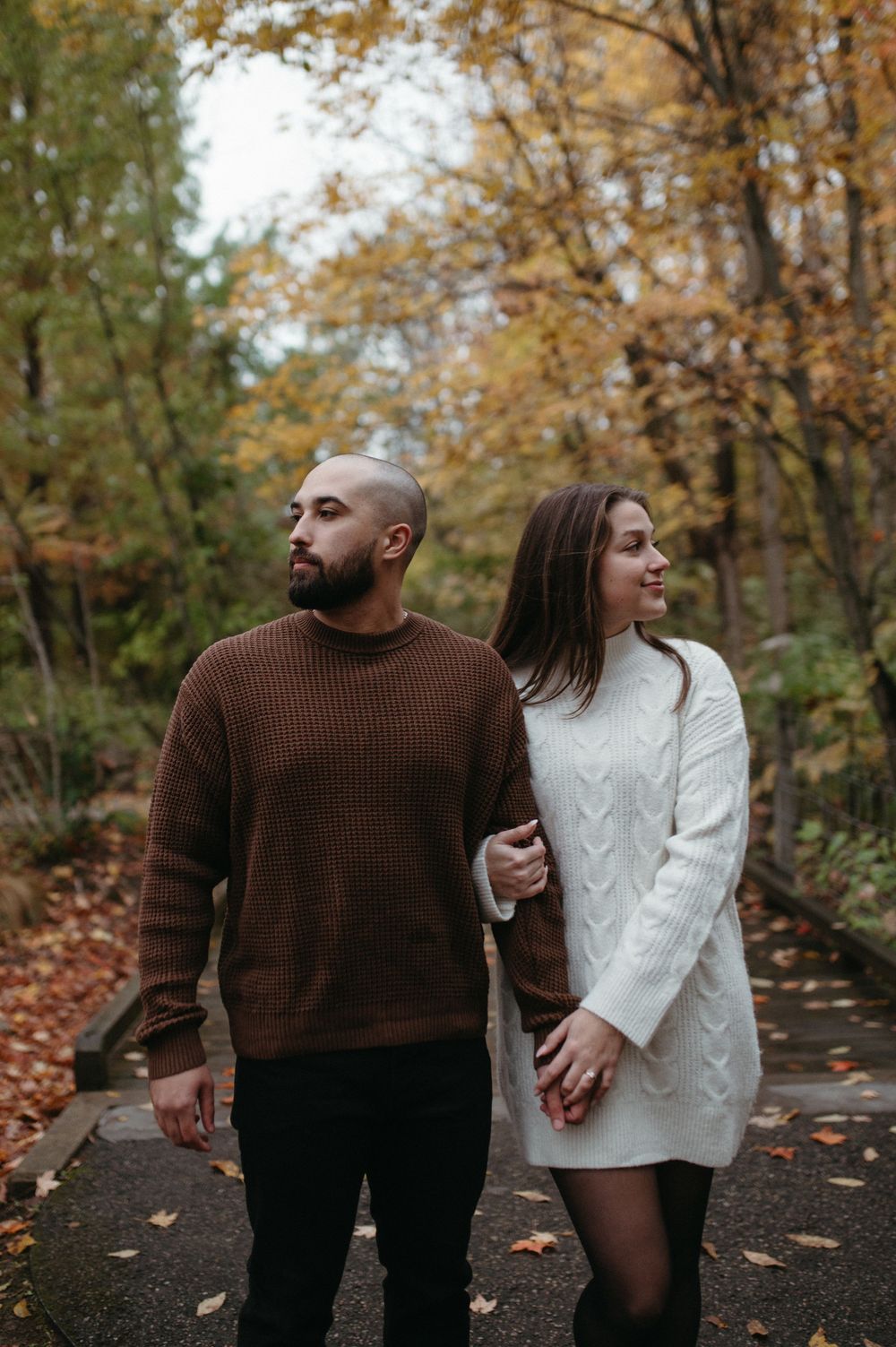A couple in cozy sweaters strolling through a fall forest.