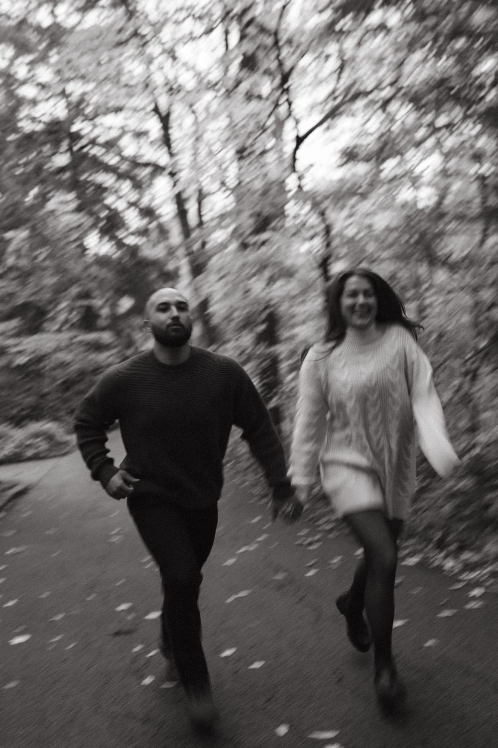 A playful black and white photo of two people running on a wooded path.