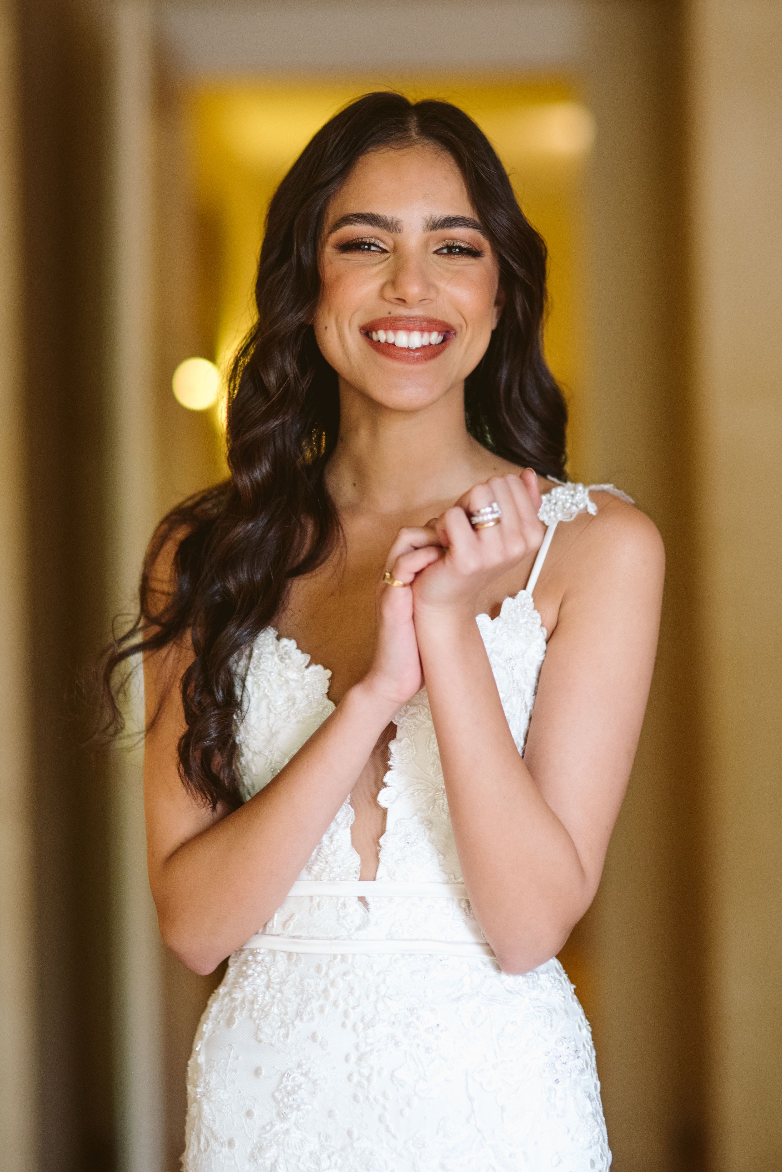 Beautiful bride in white lace gown showing engagement ring in hallway.