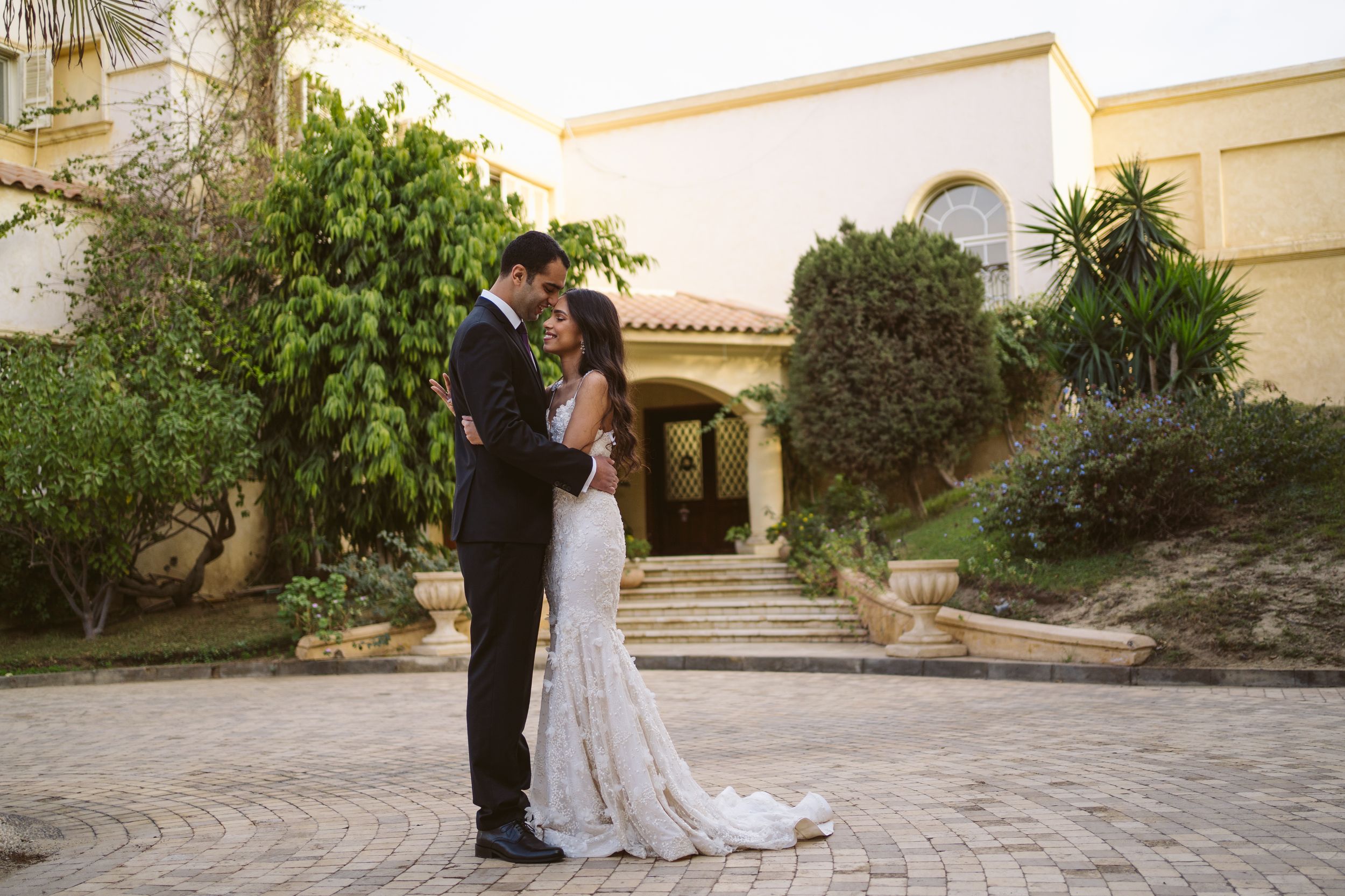 Elegant wedding couple shares intimate moment in front of Mediterranean villa entrance.