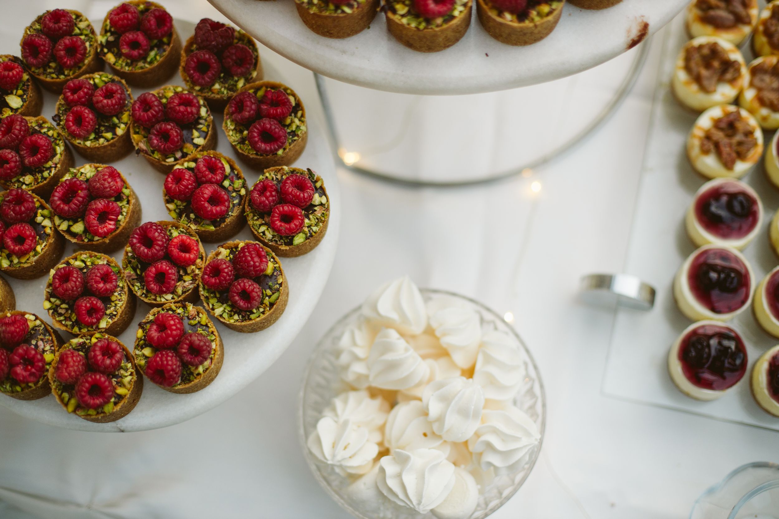 Elegant dessert table featuring raspberry tarts and meringues at wedding reception.