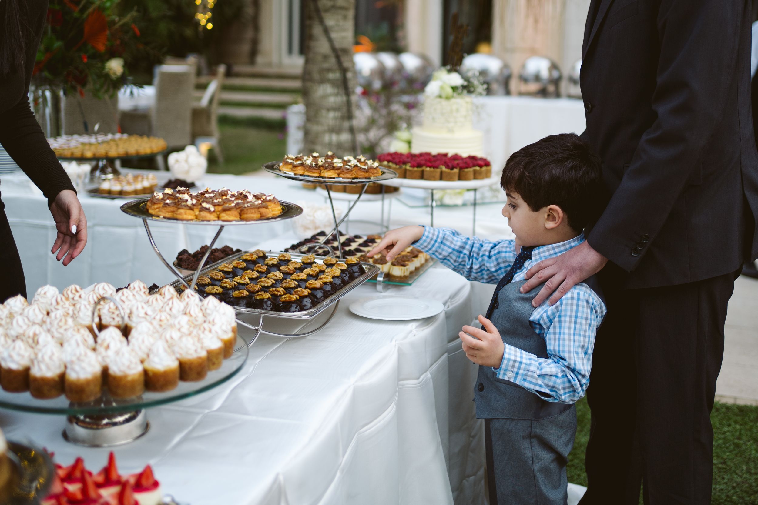 Young boy reaching for desserts at an elegant wedding reception buffet table.