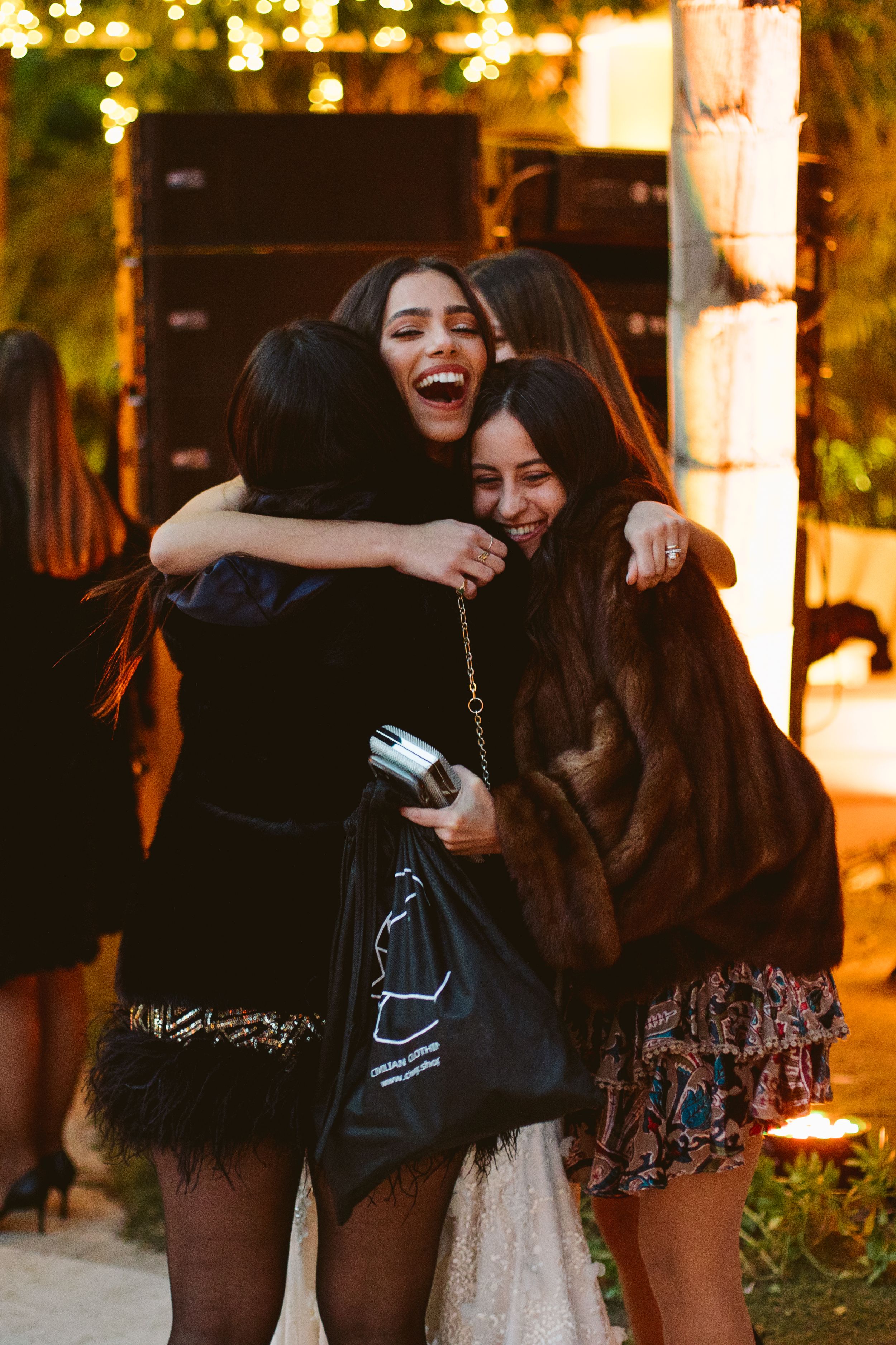 Friends sharing an emotional embrace during an evening celebration with string lights.