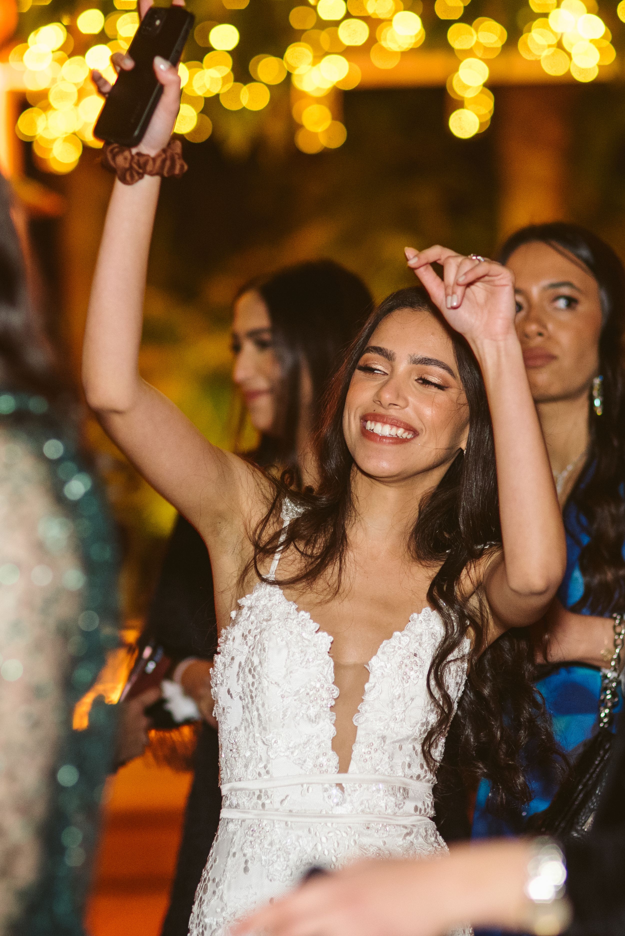 Woman in white lace dress dances joyfully under warm glowing lights at an evening celebration.