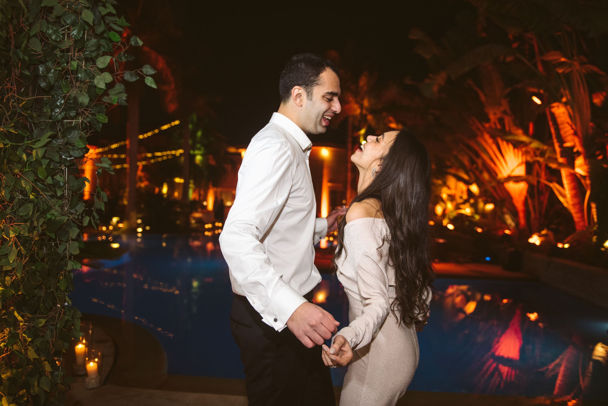 Couple dancing together at their nighttime wedding reception by a pool.