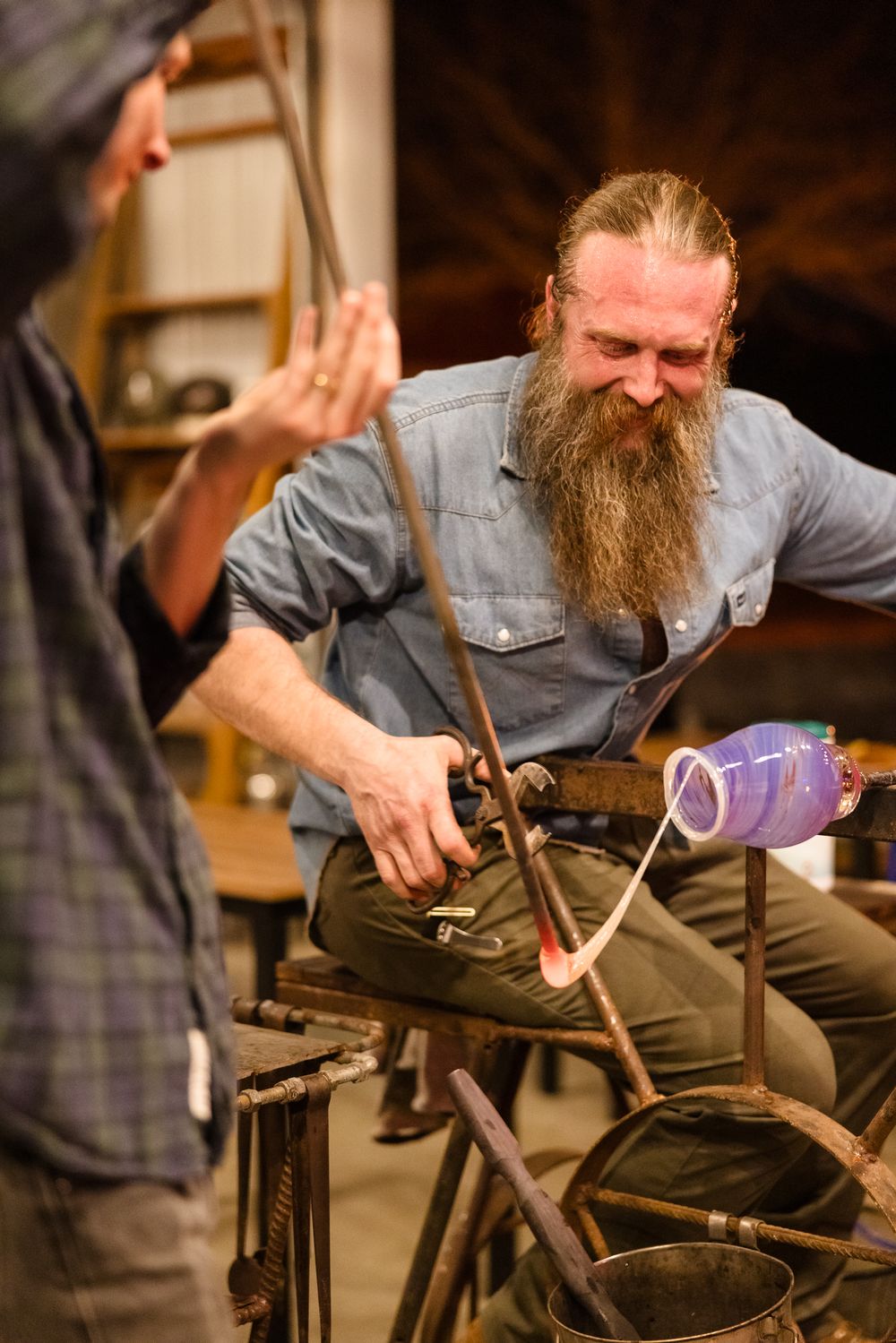 Craftsman with long beard working intently on a metal project in a workshop setting.