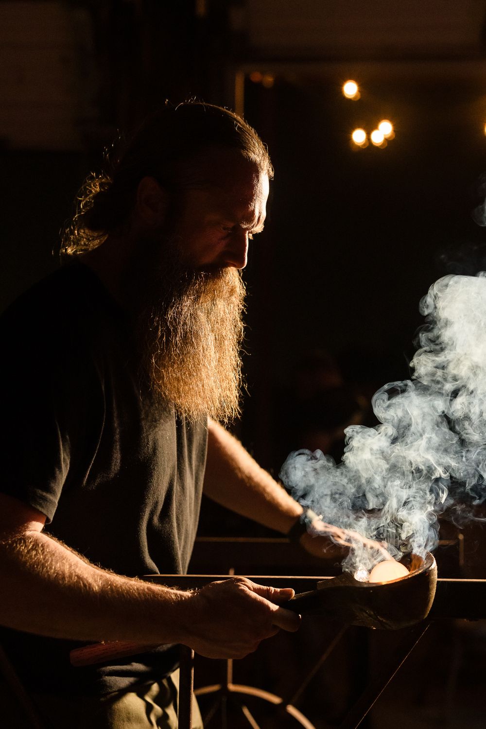 Artisan working with smoke and fire in dramatic low-key lighting conditions.