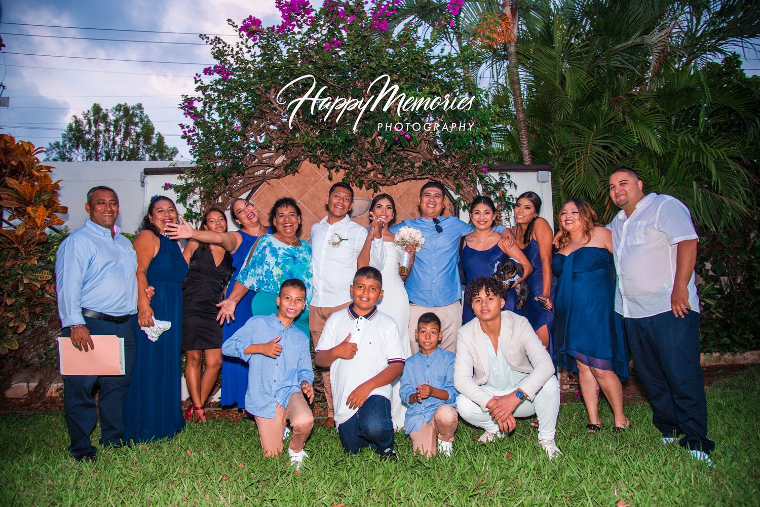 Large group photo of wedding guests in coordinated blue and white attire outdoors.