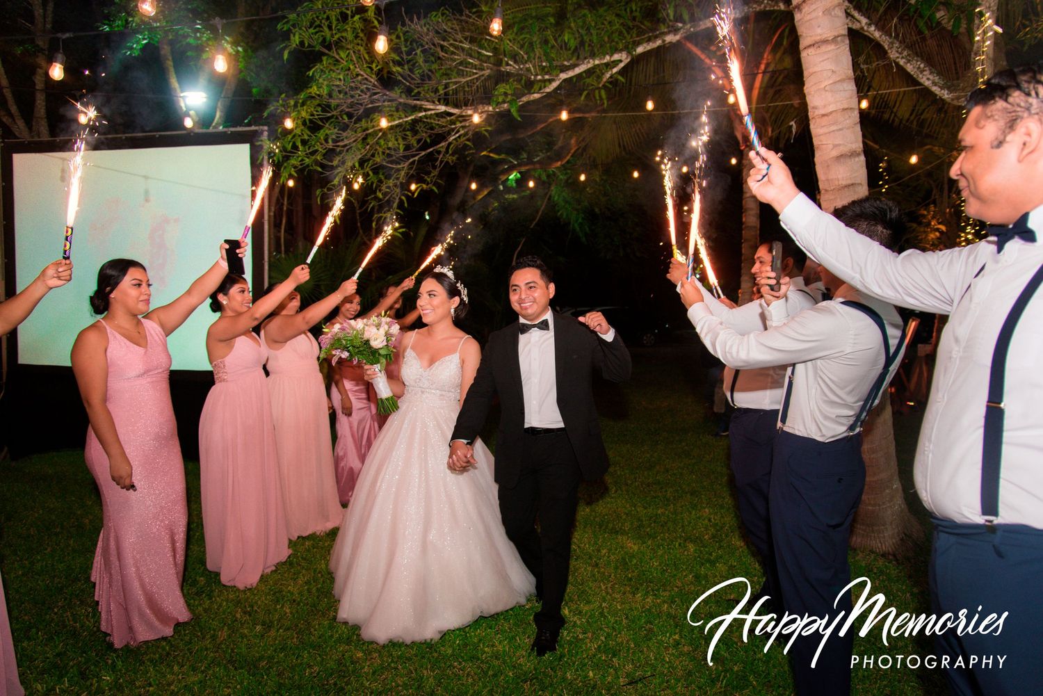 Wedding guests dancing and celebrating under twinkling lights at an outdoor evening reception.