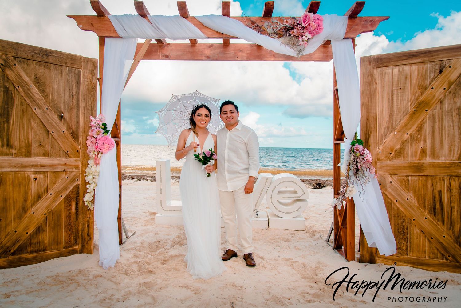 Beach wedding ceremony captured through rustic wooden doors with ocean and blue sky backdrop.