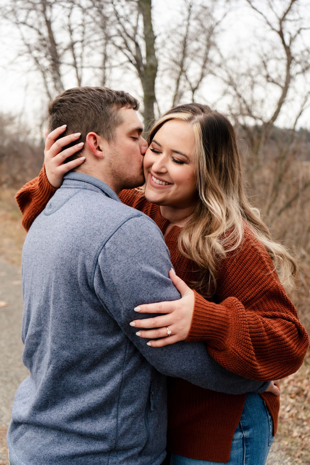 Romantic couple embraces outdoors in autumn wearing cozy sweaters in gray and rust colors.