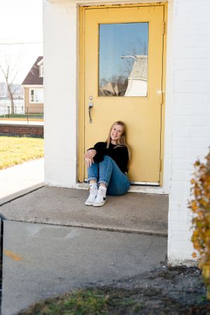 Person in casual wear sits by yellow door in outdoor setting.