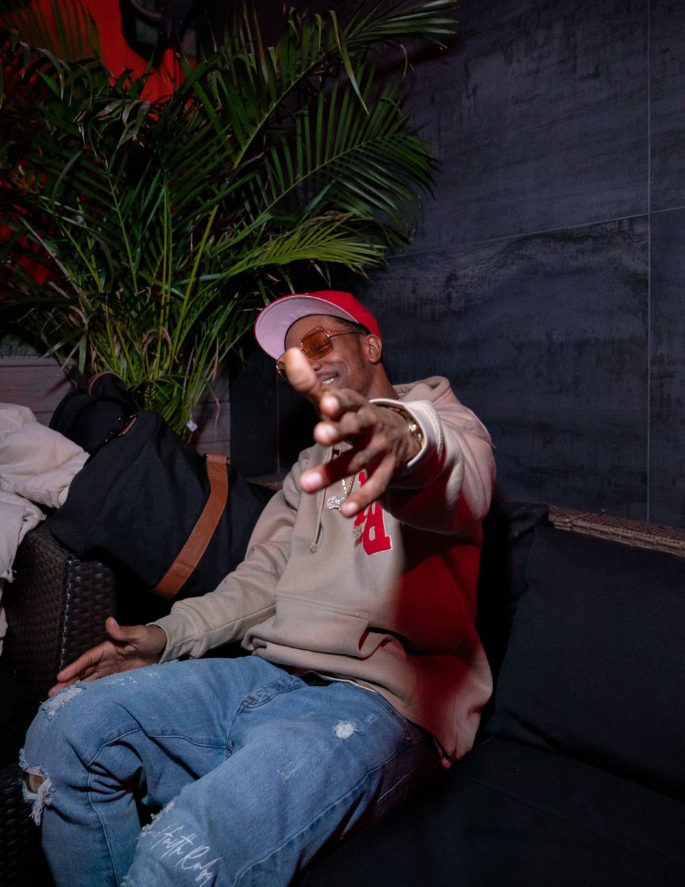 Performer in casual wear posing on couch with tropical plant in background.