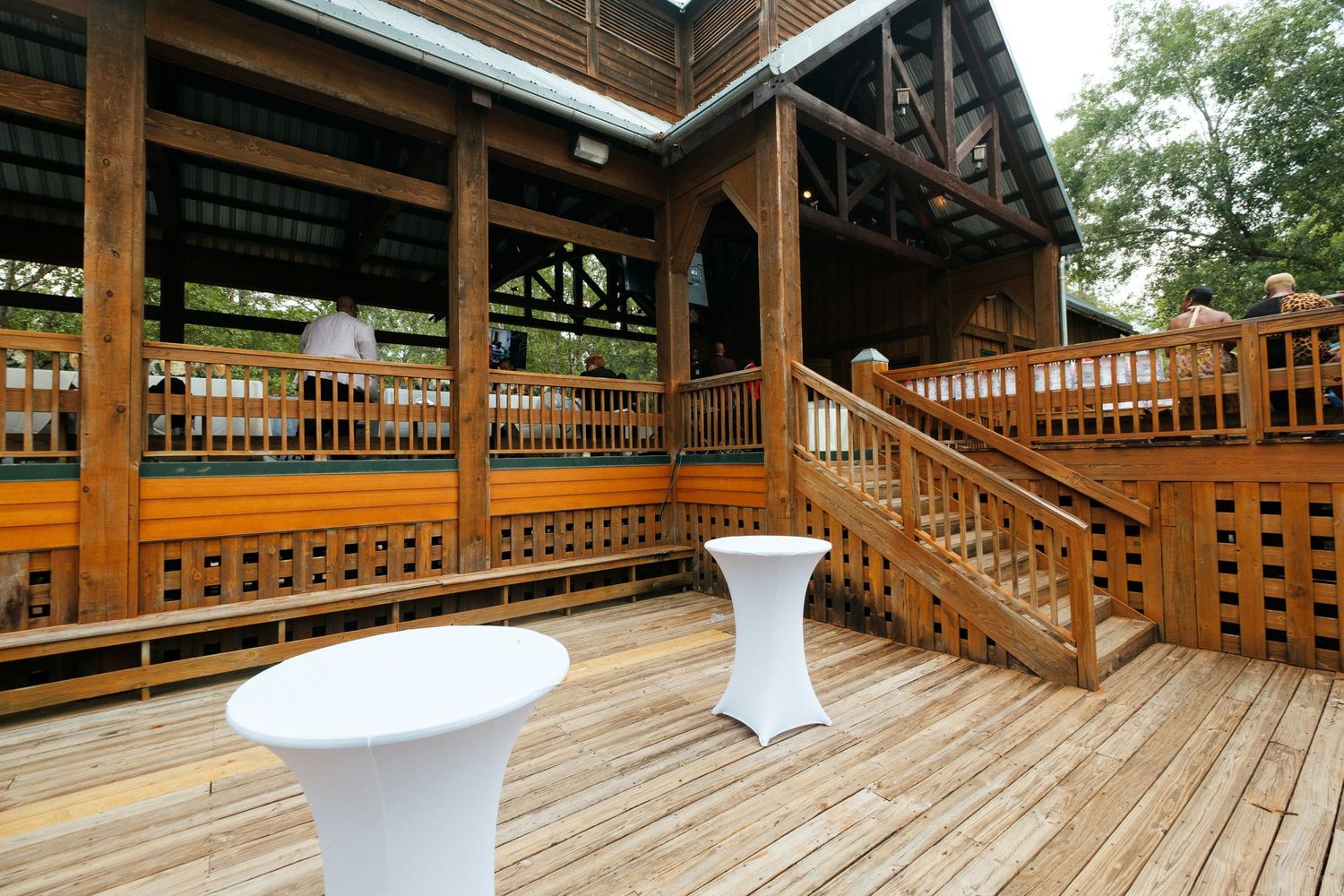 A rustic wooden deck with white cocktail tables and railing details.