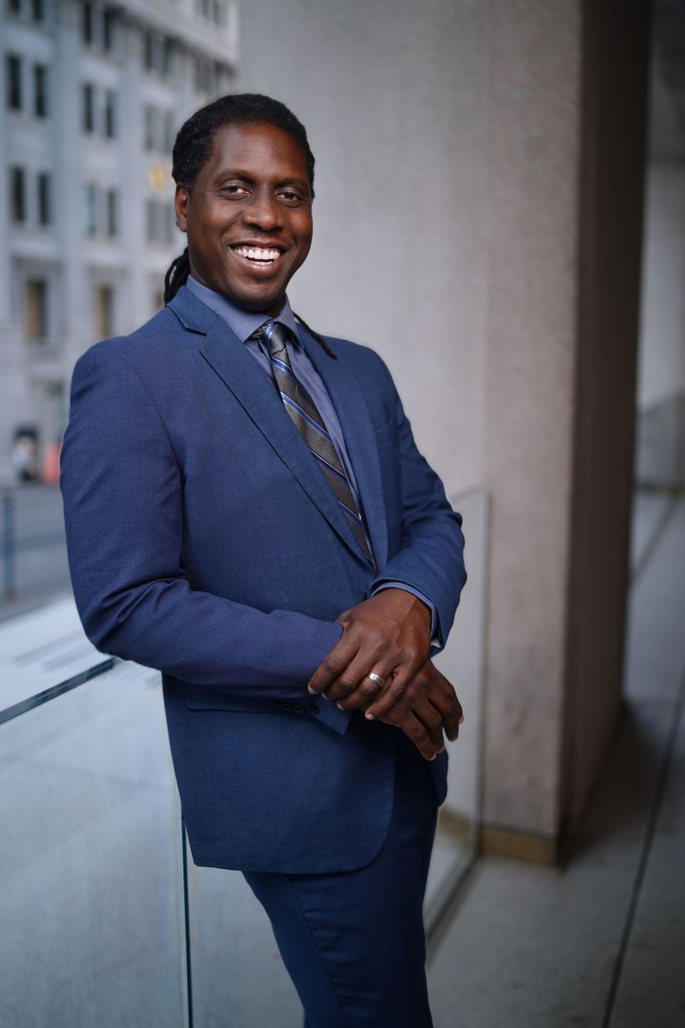 Smiling man in blue suit and tie posing outdoors near urban building.
