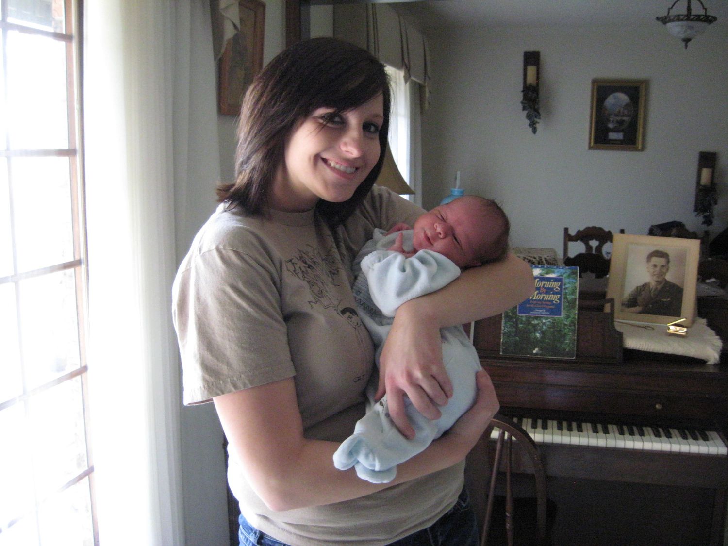 Parent holding and comforting newborn baby near piano in home setting.