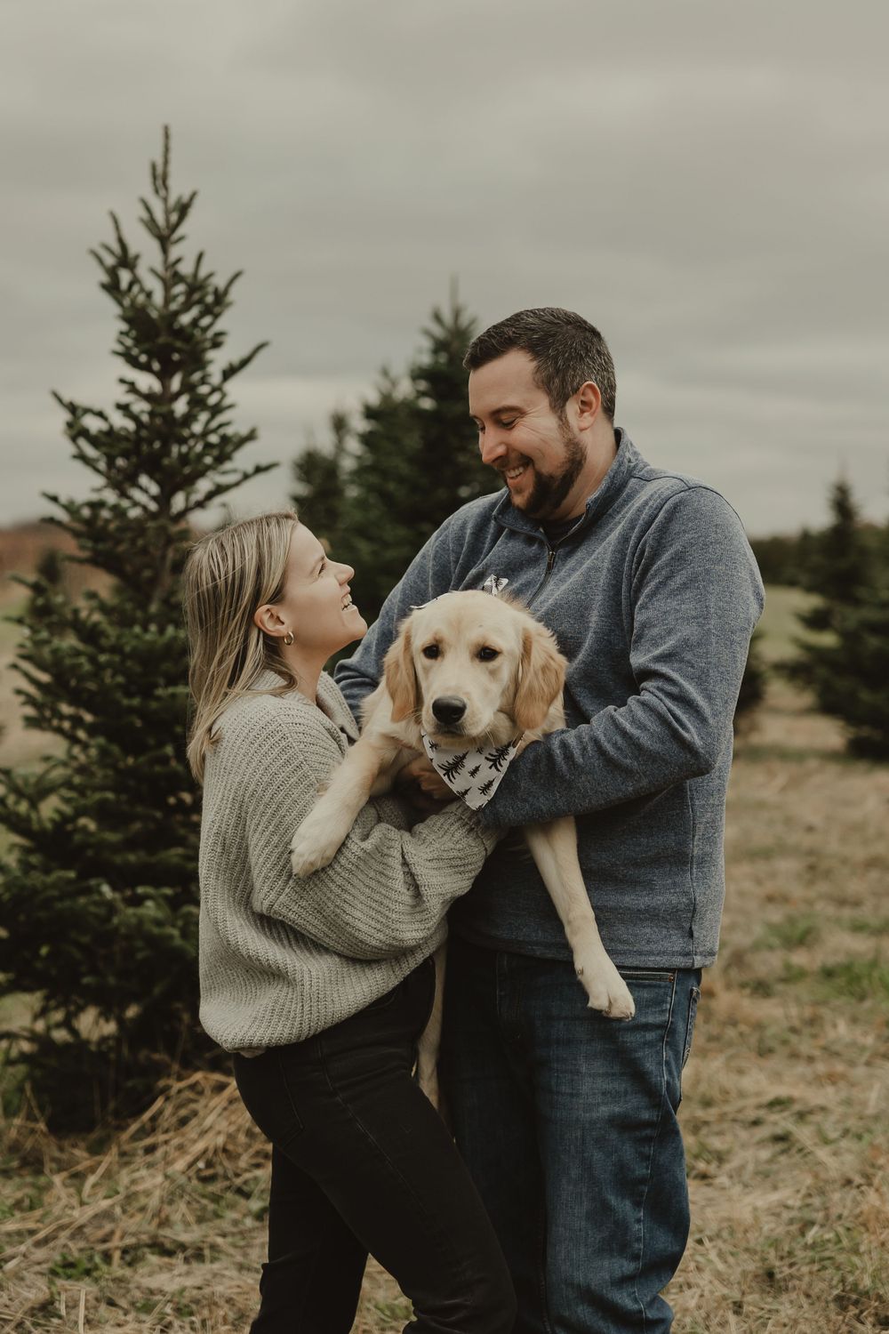 A couple sharing a joyful moment with their Labrador puppy among pine trees.