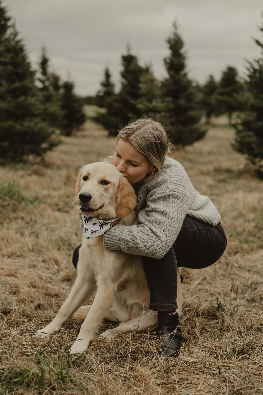 A person in a knit sweater snuggles with their golden retriever outdoors on a cloudy day.