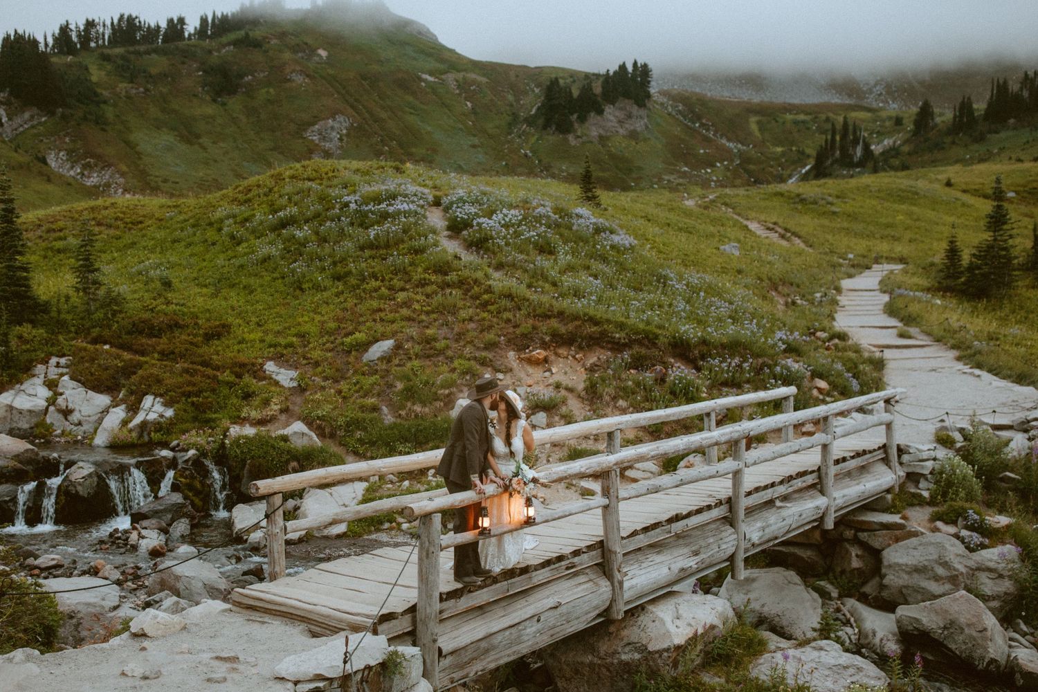 A series of wooden boardwalks wind through a misty mountain landscape with evergreen trees in the background.