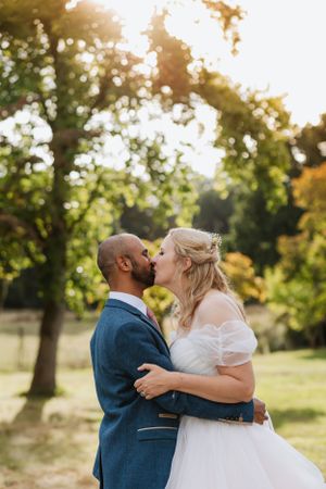 Romantic outdoor wedding portrait of couple kissing in golden sunlight.