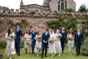 Wedding party in navy and white attire poses together against historic stone church wall.
