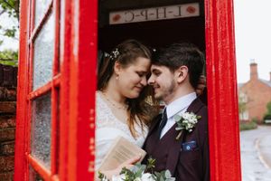 Romantic close-up of newlyweds sharing tender moment in red phone booth.