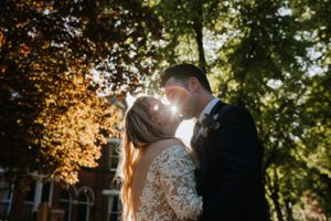 Romantic wedding couple kissing in sunlit forest with lace dress details.