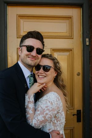 Wedding couple wearing sunglasses pose together in front of yellow door.