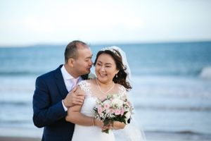 Romantic beachside wedding portrait with ocean waves in the background.
