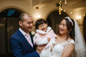 A wedding portrait of a family sharing a joyful moment indoors under arched ceilings with string lights.