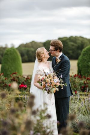 A romantic wedding portrait in a garden with blooming flowers and greenery.