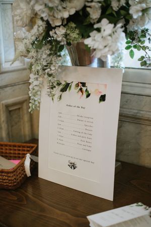 Order of the day wedding timeline printed on white paper with floral decorations on a wooden table.