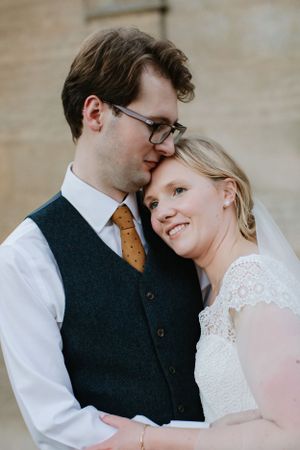 Tender wedding portrait of a couple in formal attire sharing an intimate moment against a neutral background.
