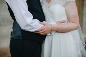 Close-up of joined hands showing wedding attire details in soft natural lighting.