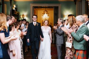 Wedding guests line up to applaud the newlyweds walking through an elegant green-walled hallway.