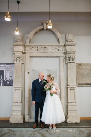 Wedding couple poses under an ornate stone archway in a historic building interior.