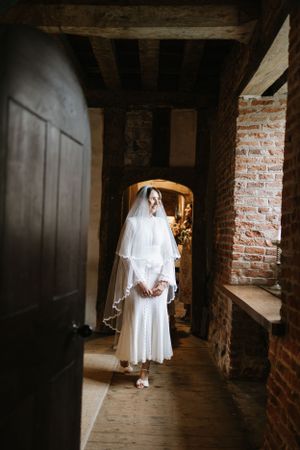 An elegant vintage-style wedding dress with flowing veil photographed in a rustic brick hallway.