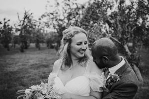 Black and white portrait of newlyweds embracing intimately in an apple orchard.
