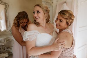 Joyful wedding preparation moment with bridesmaids helping bride get ready.