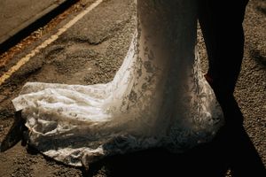 Detail shot of lace wedding dress train trailing on textured ground.