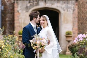 Romantic garden wedding portrait with historic brick building and blooming flowers in background.