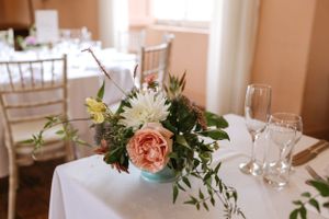 Elegant wedding centerpiece featuring blush roses and white flowers in a turquoise vase on a formal dining table.