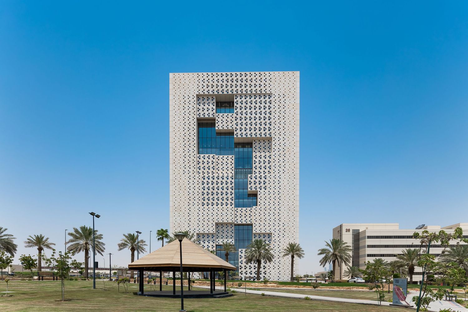 Modern architectural building with geometric facade pattern against blue sky with palm trees.