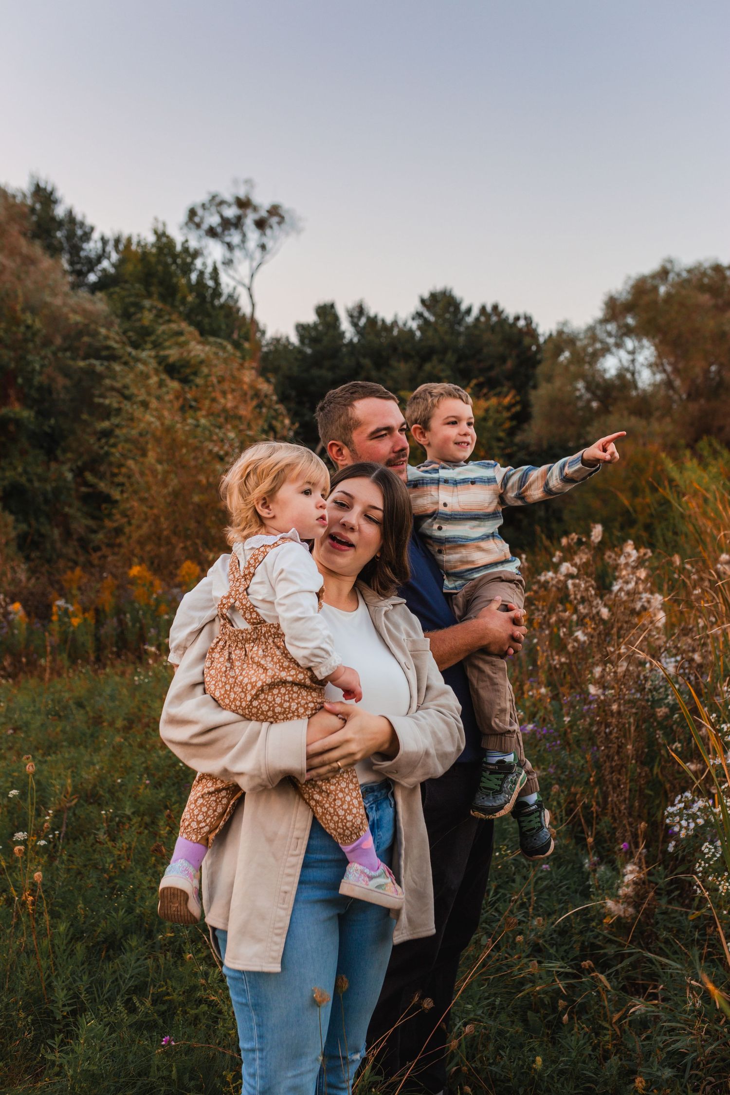 Mom and dad holding up children in a field at sunset, pointing to something in the distance