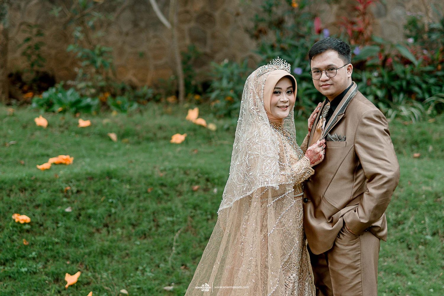 Newlywed couple in matching beige attire pose together on lawn with autumn leaves.