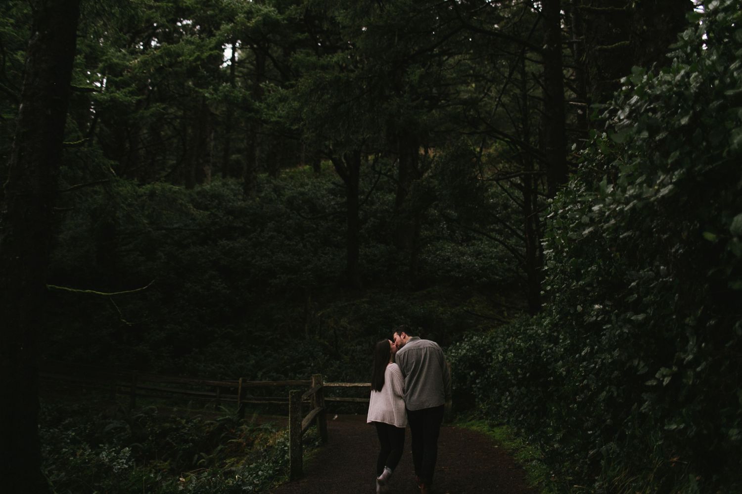 Couple walking together on a forest path surrounded by lush greenery.