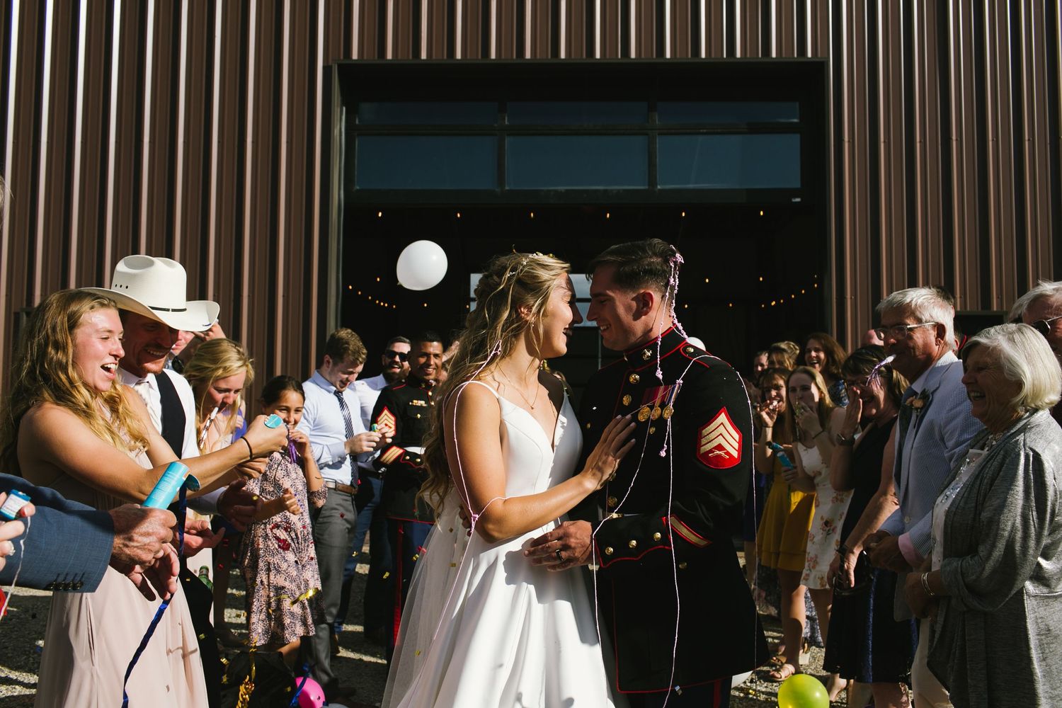 Wedding couple sharing a moment outside a modern venue with guests watching.