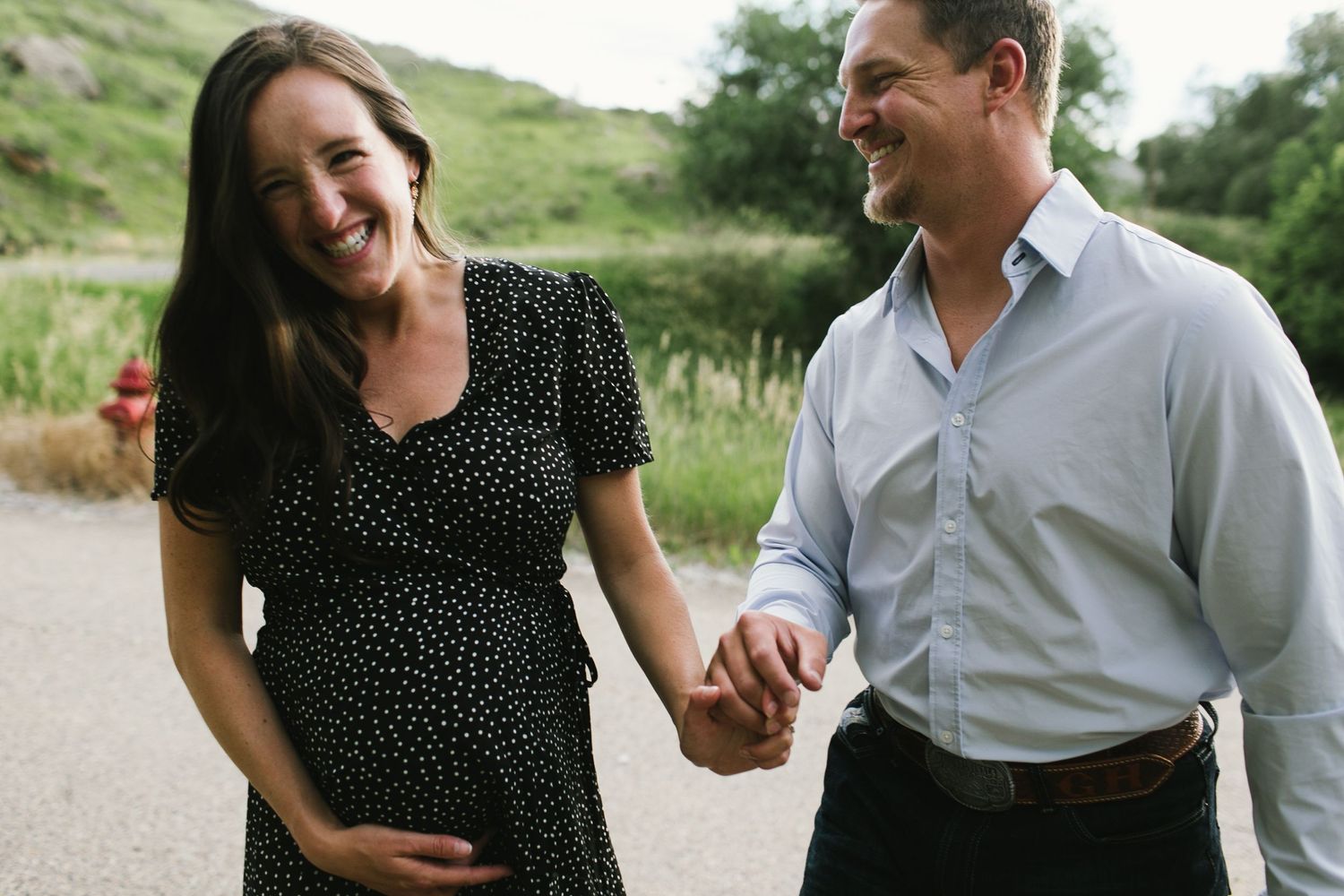 Couple in polka dot dress and white shirt laughing together on a countryside path.
